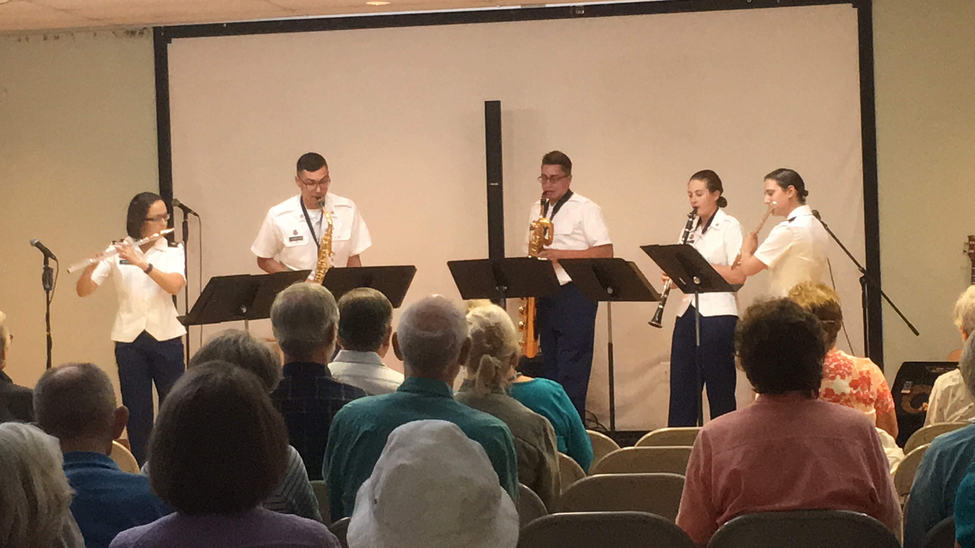 Five uniformed Army musicians performing wind instruments for an audience