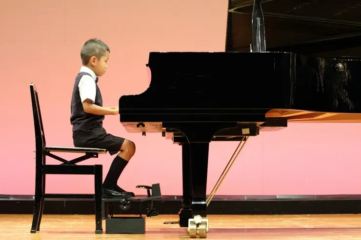 Young pianist performing at a grand piano on stage with a pink backdrop